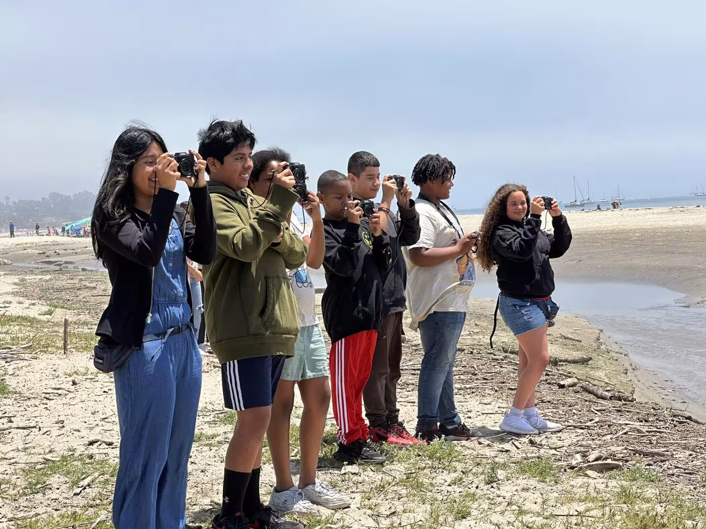 Students taking photos on a beach during a photojournalism activity.